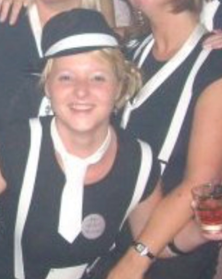 Lisa wearing a fancy dress outfit with a white tie in a crowd of people in the same outfit. She is holding a drink.